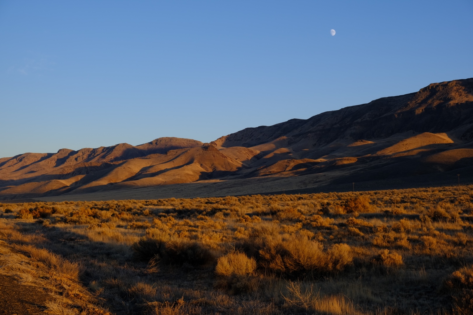 Desert mountain range at golden hour with sagebrush and crescent moon
