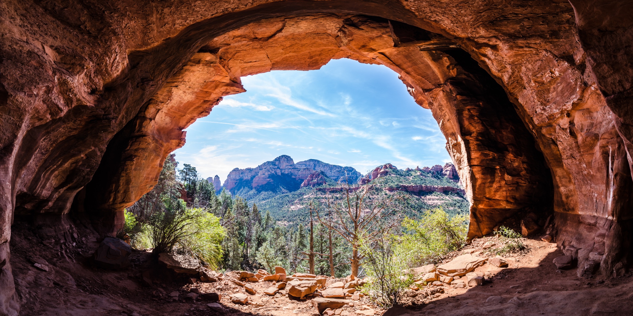 Panoramic view through a natural sandstone cave arch framing Sedona red rock formations