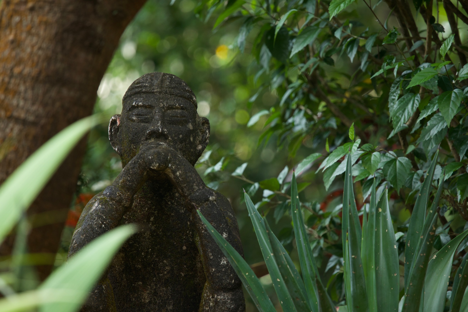 Weathered stone statue among tropical plants and greenery