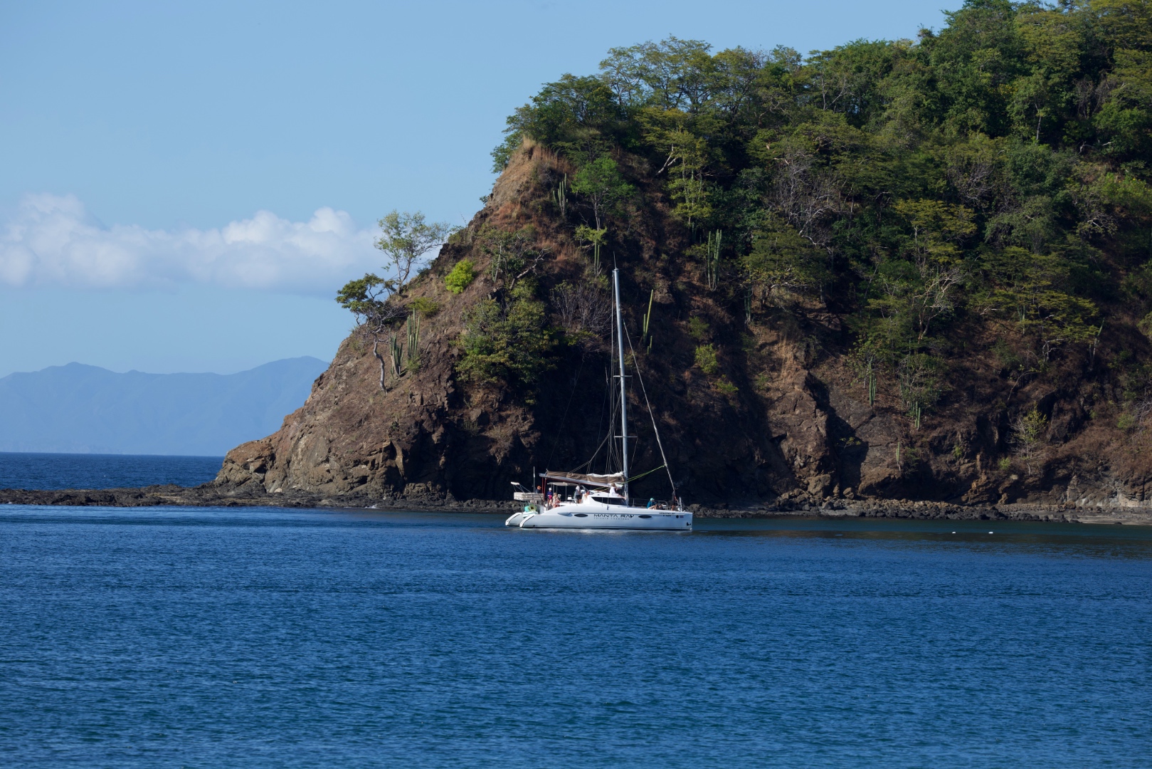 Catamaran anchored near a dramatic volcanic cliff